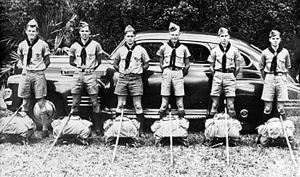 Boys lined up in front of car with backpacks and staves in front of them